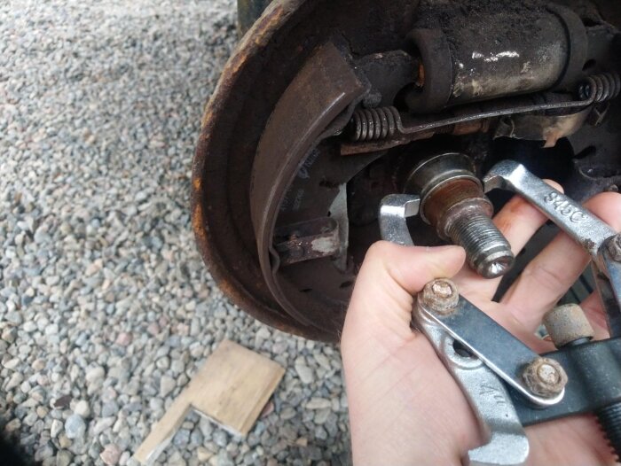 Hand håller i verktyg som försöker ta bort en lagerbana på en bromstrumma. Verktyget är placerat på en bilens urmonterade hjultrumma.