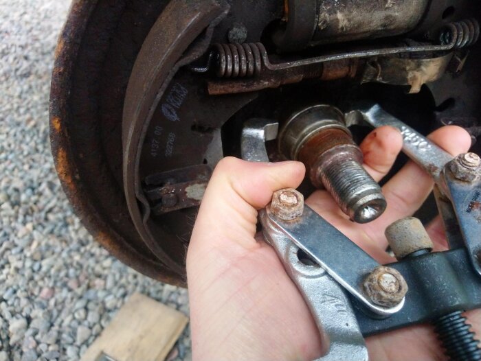 Närbild av en parkeringsbroms med en hand som håller en avdragare runt ett fastnat hjullager i en trumma, streckad av lagerbanan.