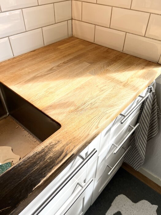 Bänkskiva i ek som delvis har slipats, visar kontrast mellan mörkare oljad yta och ljusare omålad träyta, bredvid diskho i kök.