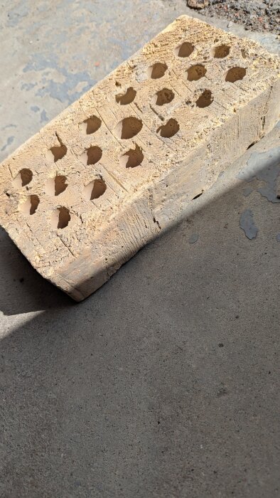 Tegeltegelsten med hål, placerad på en betongyta i ett renoveringsprojekt, med avsikt att montera TV och hyllor.