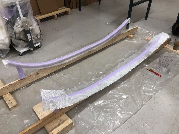 Två xps-balkar klädda i glasfiber vilar på trästöd för härdning; del av ett byggprojekt för att styva upp en dörrkarm.