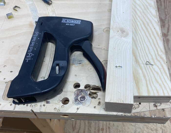Svart häftpistol av märket J.C. Schwarz på ett bord, med två synliga klammer i träbredvid.