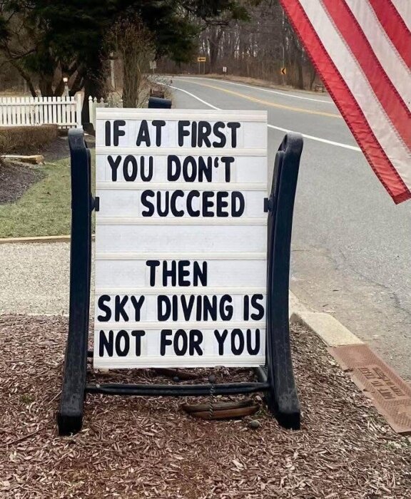 Skylt vid landsväg med texten: "If at first you don't succeed then sky diving is not for you", bredvid en amerikansk flagga.