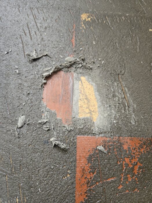 En närbild av en yta med klistrigt, gummiaktigt material som har skrapats bort delvis, avslöjande orange och gul färg under.