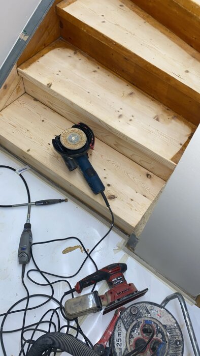 Trätrappa under renovering med olika verktyg som slipmaskin och såg på plats.