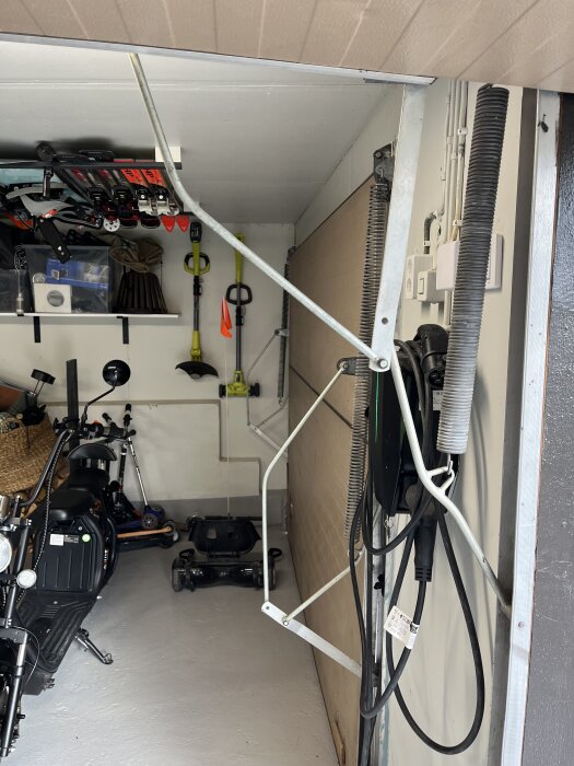 Garageinteriör med äldre port, elverktyg på hyllor, cykel och annan utrustning synliga.