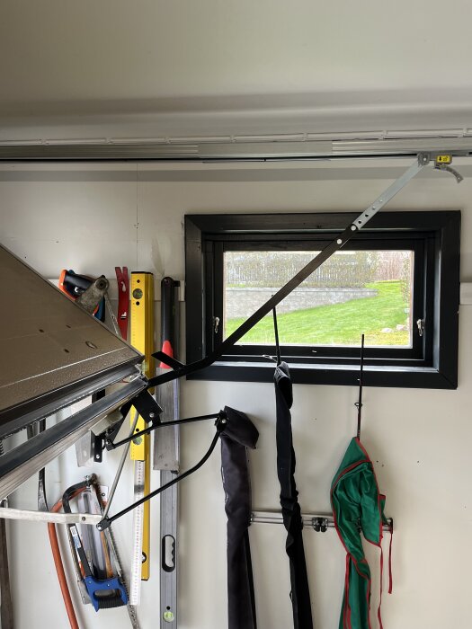 Inifrån av en äldre garagedörr med verktyg och förvarade kläder hängande på väggen, innan byte av porten.