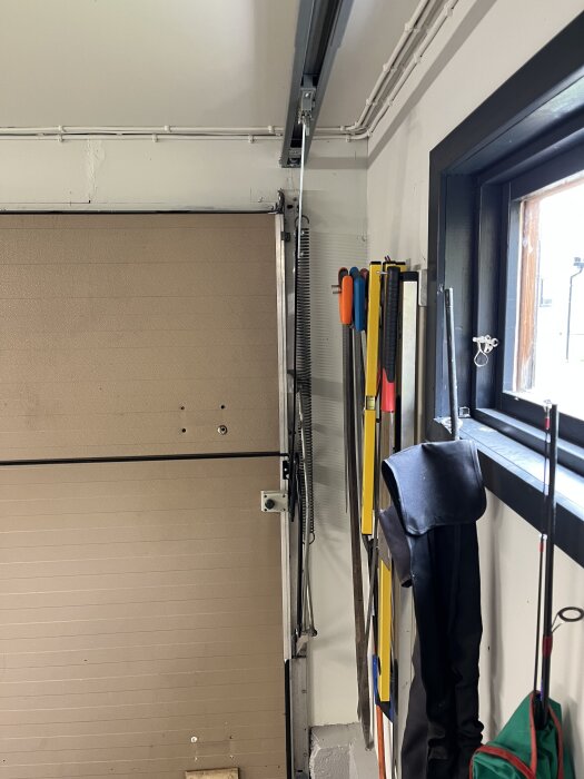 En garageport från insidan, omgiven av väggskenor och verktyg som hänger på väggen.
