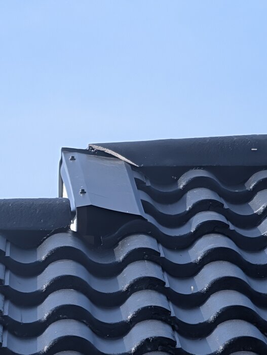 Tegelbelagt tak med kapade pannavslut vid en dal; plåten täcker inte helt. Vindskiveplåtens ände syns. Problem med tätning och vatteninträngning.