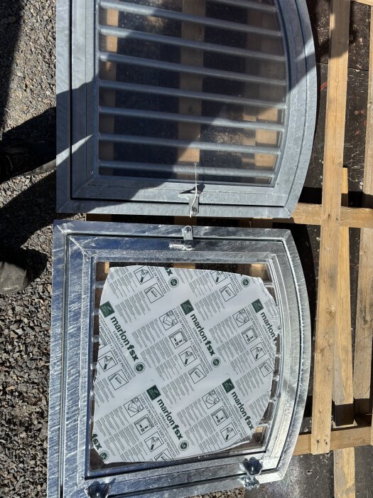 Två fönster, ett med blank och ett med matt varmgalvaniserad yta, liggande på marken.