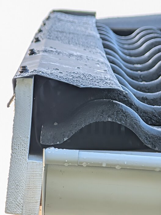 Takfot med regndroppar på vindskiveplåt och tegelpannor, visar övergången mellan materialen.