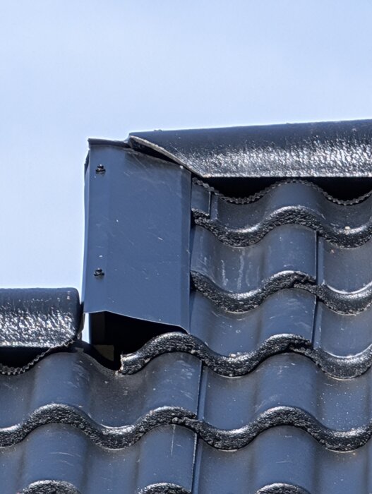 Detalj av tak med mörka tegelpannor och vindskiveplåt som möts vid kanter.