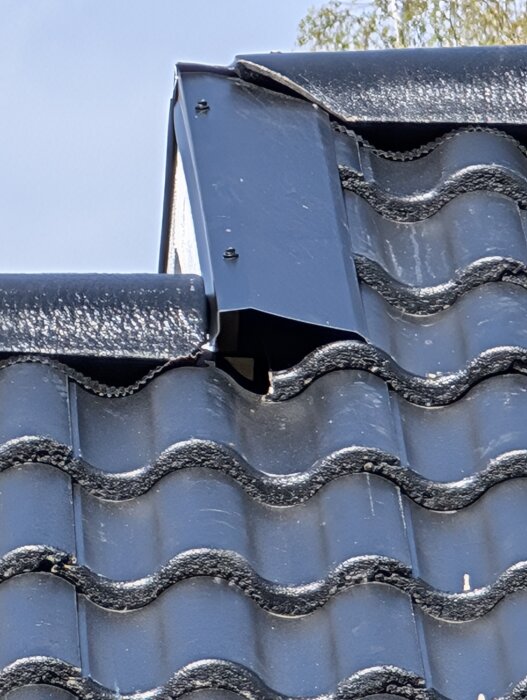 Bilden visar ett tak med svarta tegelpannor där vindskiveplåt övergår från takkant till beklädnad. Plåten är monterad med skruvar.