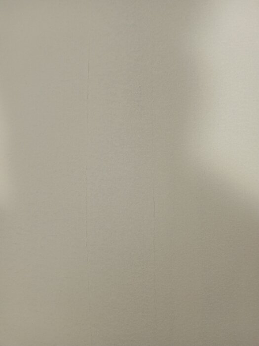 Närbild av en gipsvägg med tunna sprickor längs en pappremsa som limmats med våtrumslim.