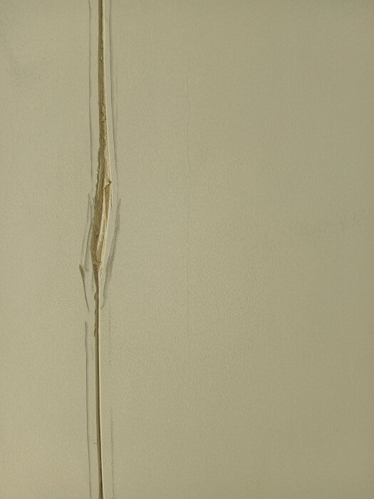 Spricka i en pappremsa på ett gipstak, orsakad av limning med våtrumslim. Remsan har lossnat något längs kanten och visar tecken på felaktig applicering.