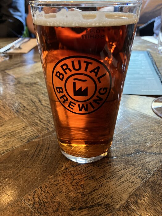 Ett glas med bärnstensfärgad öl från Brutal Brewing på ett träbord.