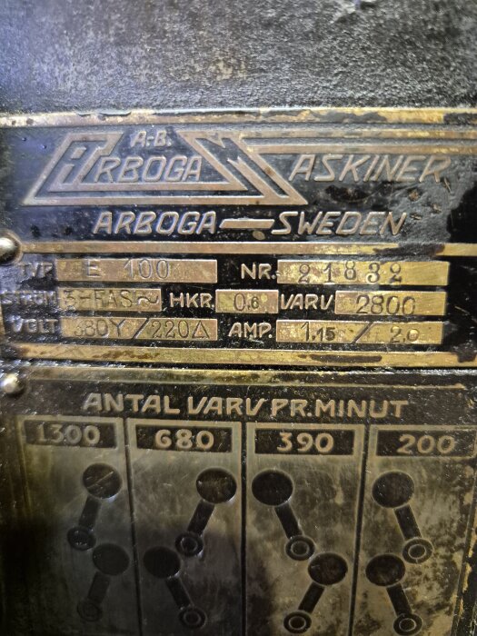 Skylt på maskin från AB Arboga Maskiner med modellnummer E 100 och serienummer 21832, visar teknisk specifikation och varvtal per minut.