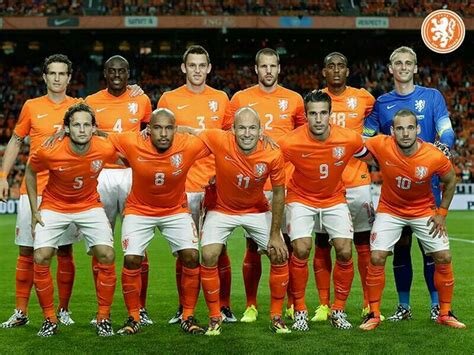 En grupp fotbollsspelare i orangea landslagsdräkter poserar på en fotbollsplan inför en match.