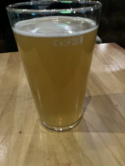 Ett glas med ljus öl på ett träbord.