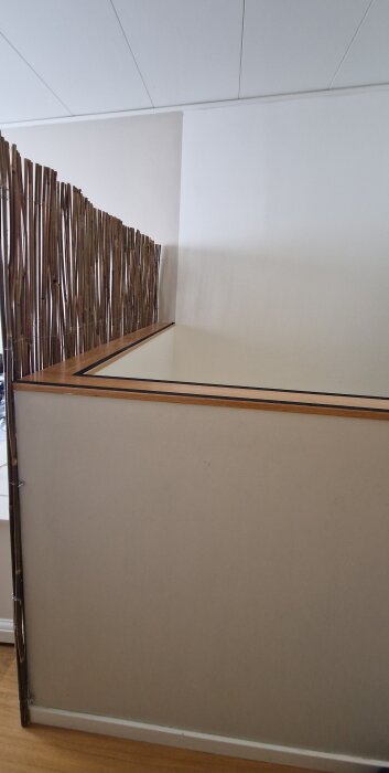 Halvvägg mot trappa med brun och vit färg, intill ett snedtak. Vertikala stavar längs ena sidan.