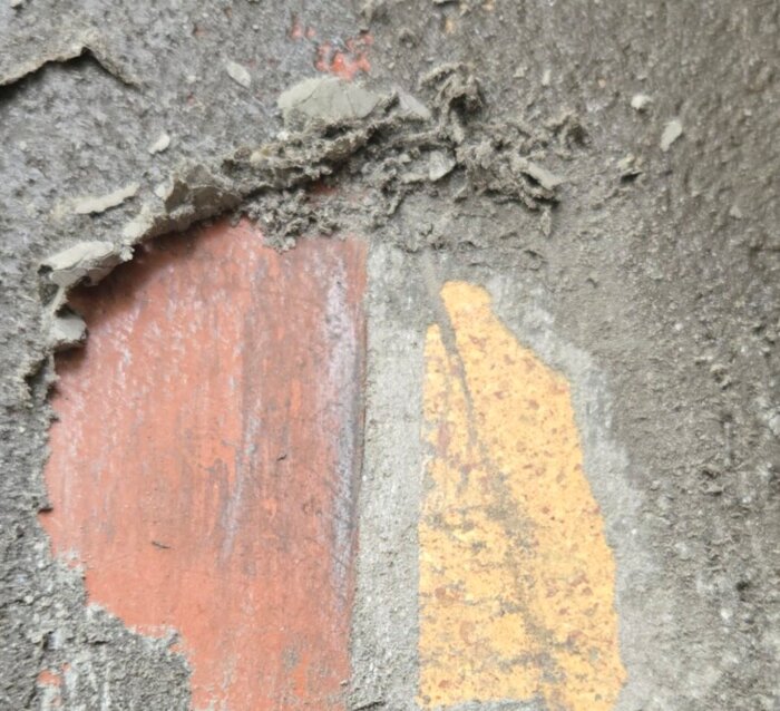 Avflagrat lager av färg och mineralbaserat material på en vägg, med synlig röd och gul underfärg.