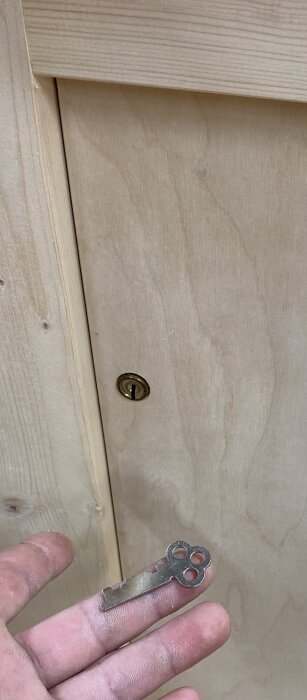 Hand som håller en nyckel framför en låsbar lucka på en medtagbar bänk. Pinnarna är symmetriska och luckan har ett tvåtillhållarlås.