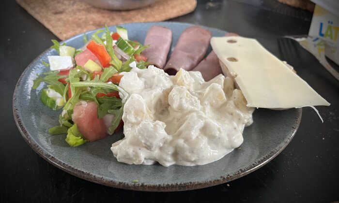 Tallrik med rostbiff, potatissallad, grönsallad med tomat och gurka, samt bröd med ostskiva.