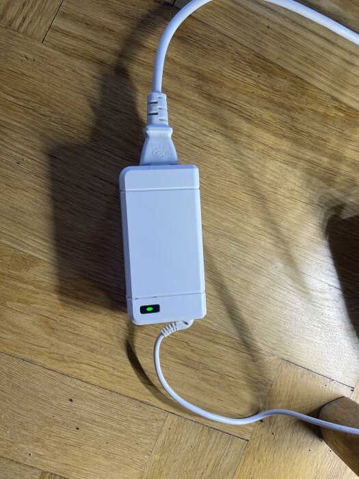 Vit adapter på trägolv med två anslutna kablar, en på vardera sidan.
