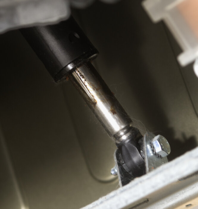 Närbild på nedre delen av en läckande stötdämpare i en tvättmaskin.