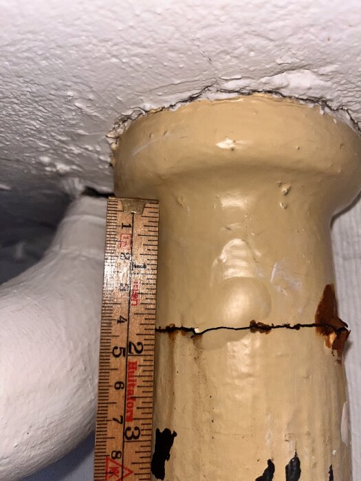 Närbild på sprucket avloppsrör nära taket med linjal för mått.