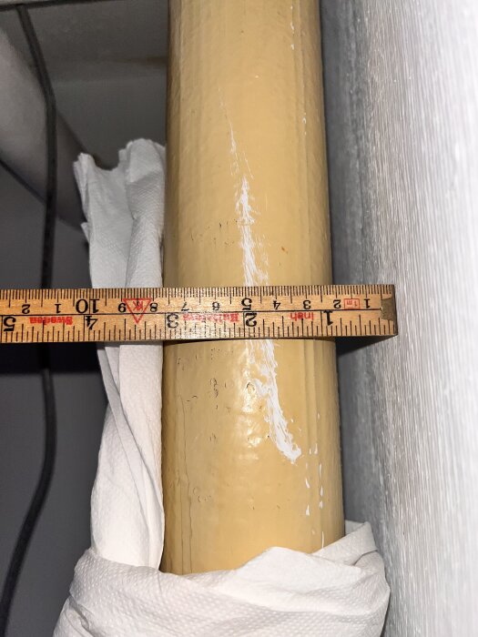 Gult avloppsrör i källare med måttband som visar 69mm ytterdiameter, omgiven av papper.