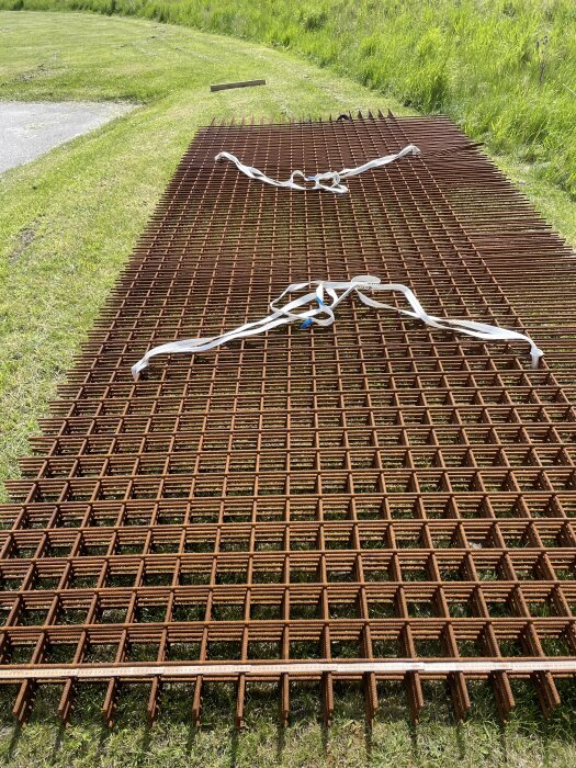 Rostiga armeringsmattor ligger på gräs med spännband ovanpå, redo för användning i byggprojekt.