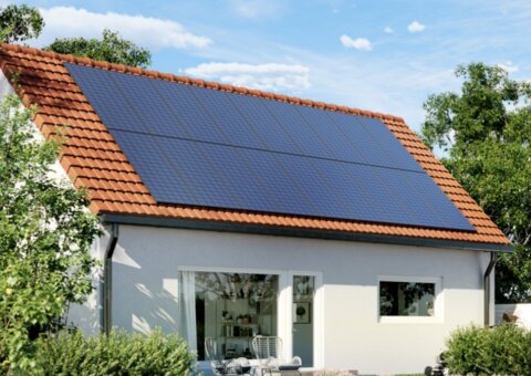 Solcellspaneler monterade på ett rött tegeltak på ett hus i soligt väder med gröna träd i bakgrunden.