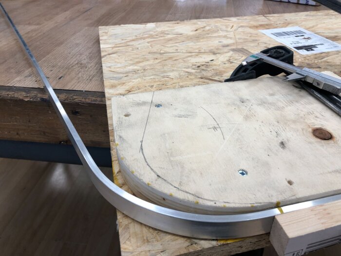 Aluminiumplatta bockad över en träjigg för att göra en 90-gradersram hör till ett fönsterprojekt, med tvingar och verktyg synliga på arbetsbänken.