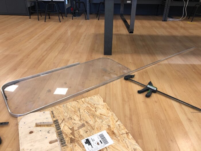 Aluminiumram och polykarbonatpanel ligger på golvet i en verkstad, med verktyg och arbetsbänk i bakgrunden.