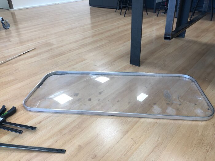 Stor polykarbonatruta med aluminiumram på trägolv; en del av ett byggprojekt för tvåglasfönster till husvagn. Verktyg och material ligger bredvid.