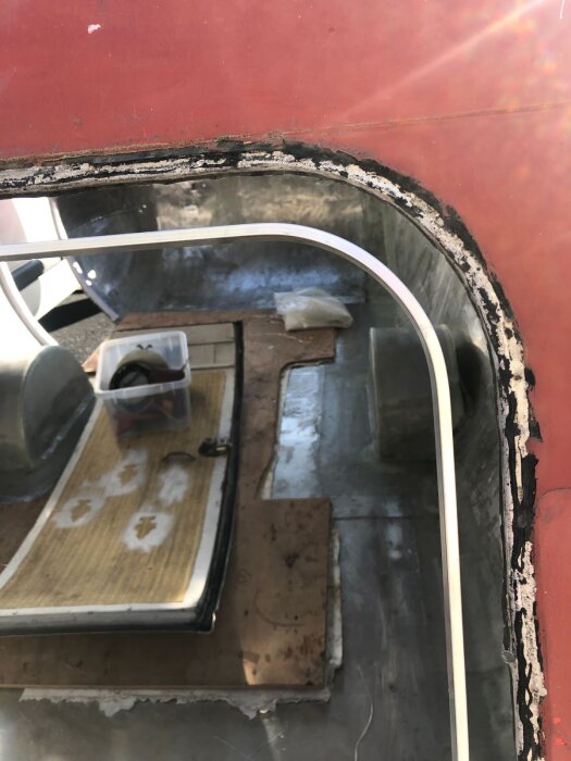 Fönsteröppning i husvagn med röd kaross, aluminiumram monterad, inuti syns verktyg och material för byggprojekt.