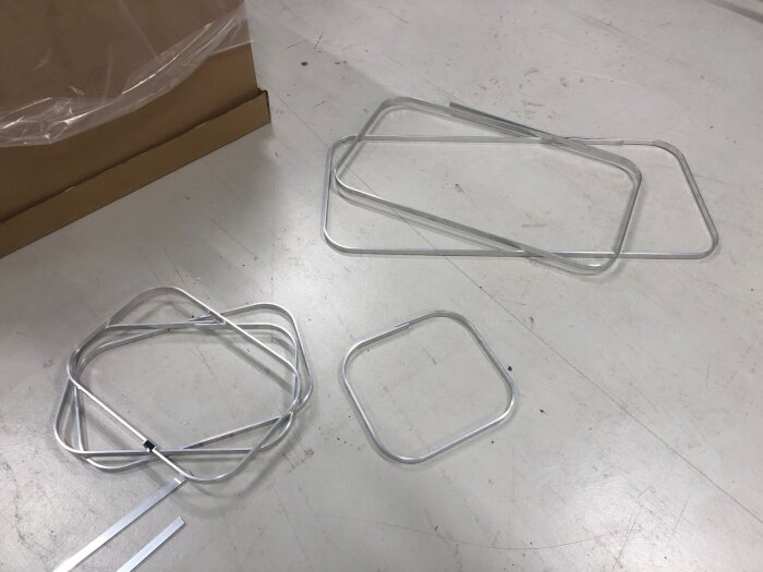 Aluminiumramar i olika storlekar för fönsterprototyper ligger på ett golv bredvid en kartong.