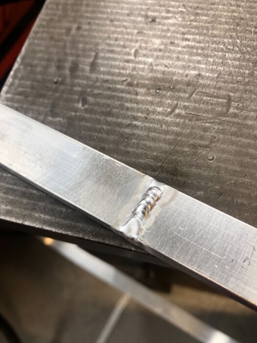 Aluminiumsvetsning på en plattstång med synliga, smala svetsfog på en verkstadsbänk.