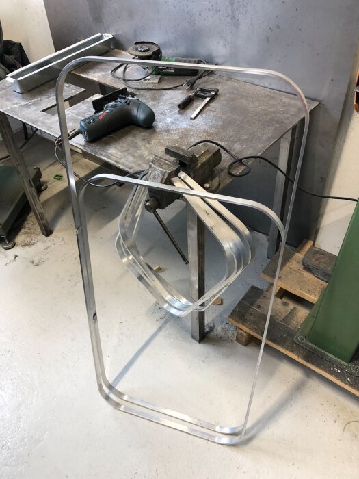 Aluminiumbockad ram för husvagnsfönster står lutad mot ett arbetsbord med verktyg i en verkstad.