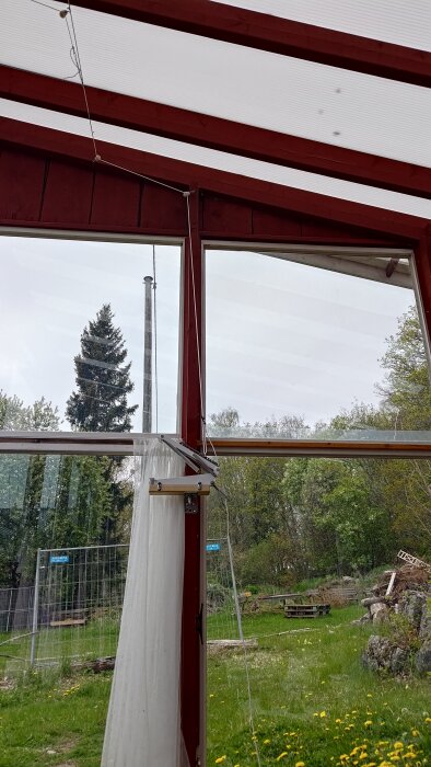 Växthus med automatiserade vädringsluckor, röd träkonstruktion och utsikt över grönskande trädgård.