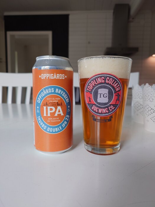 Oppigårds Thurbo Double IPA burk bredvid ett glas med samma öl, båda står på ett vitt bord i ett modernt kök.