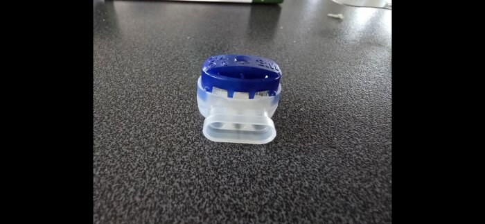 Förgreningsdosa i plast med plats för tre kablar, blå och genomskinlig, på mörkgrå yta.