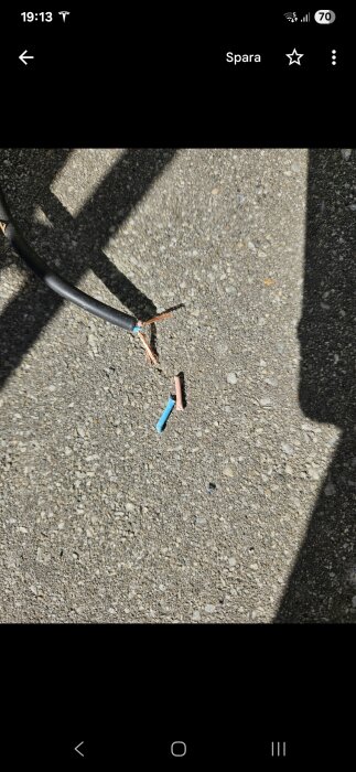 Bruten kabel med blottade kopparledare, två färgade trådar (blå och brun) synliga, på en grov yta.