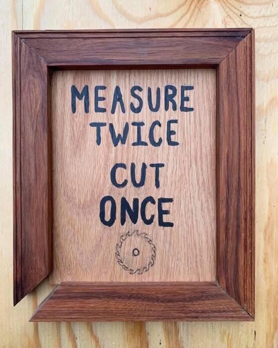 Träram på väggen med orden "Measure Twice Cut Once" och en ritning av ett sågblad.