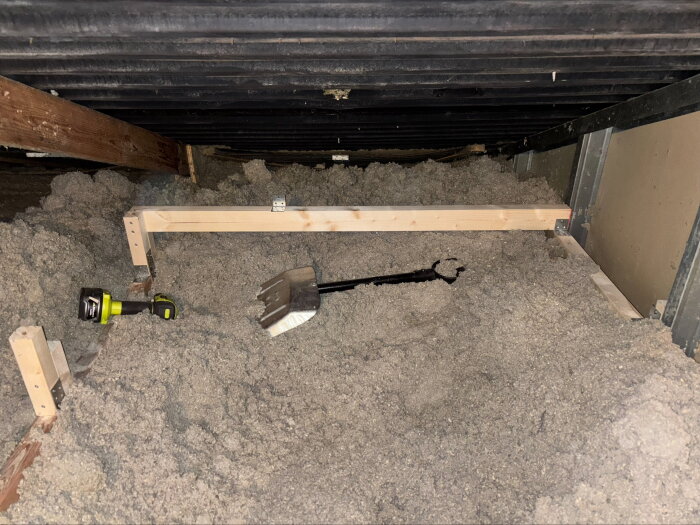 Vind med isolering och synlig takkonstruktion, träreglar, en spade och ficklampa. Visar insidan av taket och byggets skick.