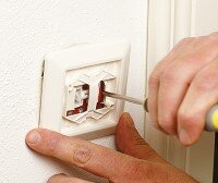 Person reparerar ett eluttag med en skruvmejsel i ett hem.