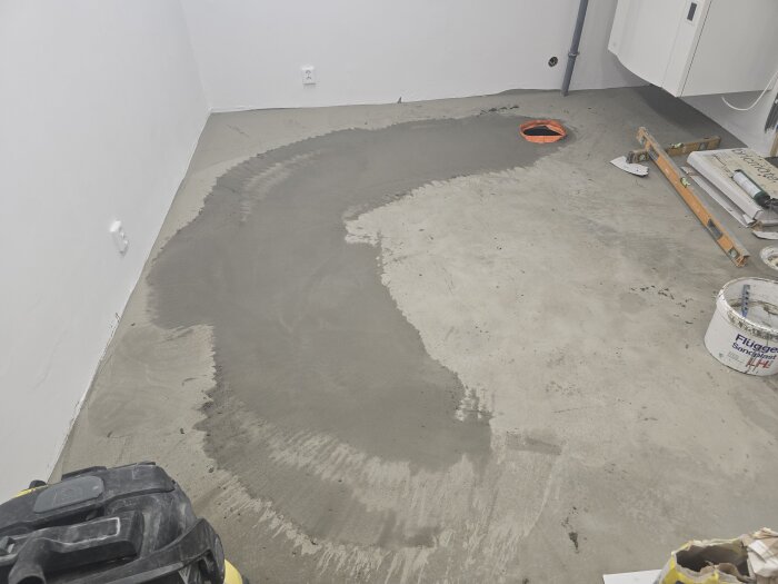 Flytspackel applicerat på ett betonggolv, verktyg och byggmaterial ses i bakgrunden, redo för plattsättning i maskinrummet.