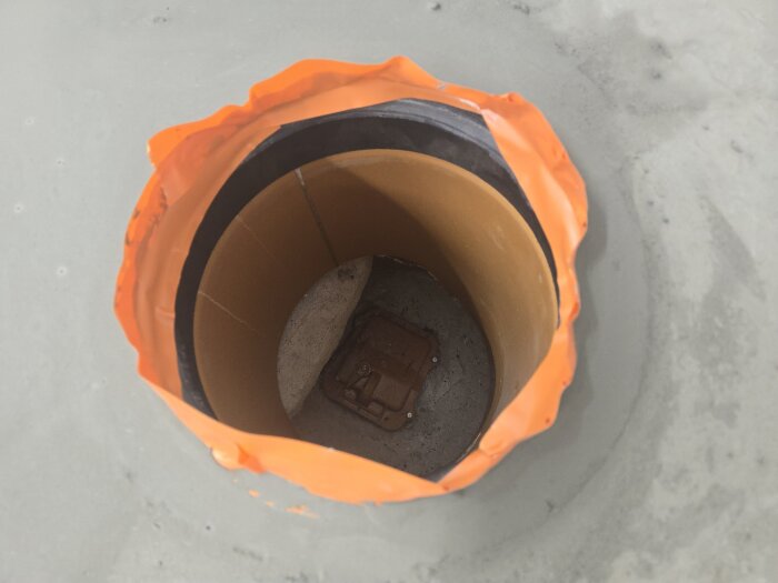 Inspektionslucka i golv omgiven av flytspackel, med ett orange och svart tätningsmaterial runt öppningen.