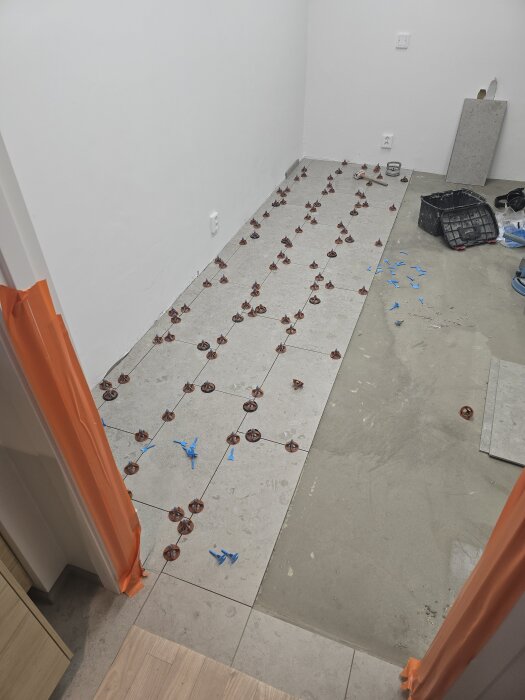 Nyplattat duschrum med grå klinkerplattor och nivåklossar. Omgivande väggar är standardvitt. Verktyg och material syns i bakgrunden.